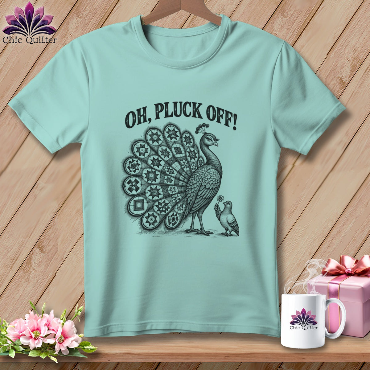 Light blue t-shirt featuring a peacock with a quilted tail, a small bird, and the text Oh Pluck Off.