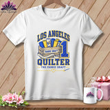 White t-shirt with a blue and yellow Los Angeles Quilter graphic hanging on a wooden background.