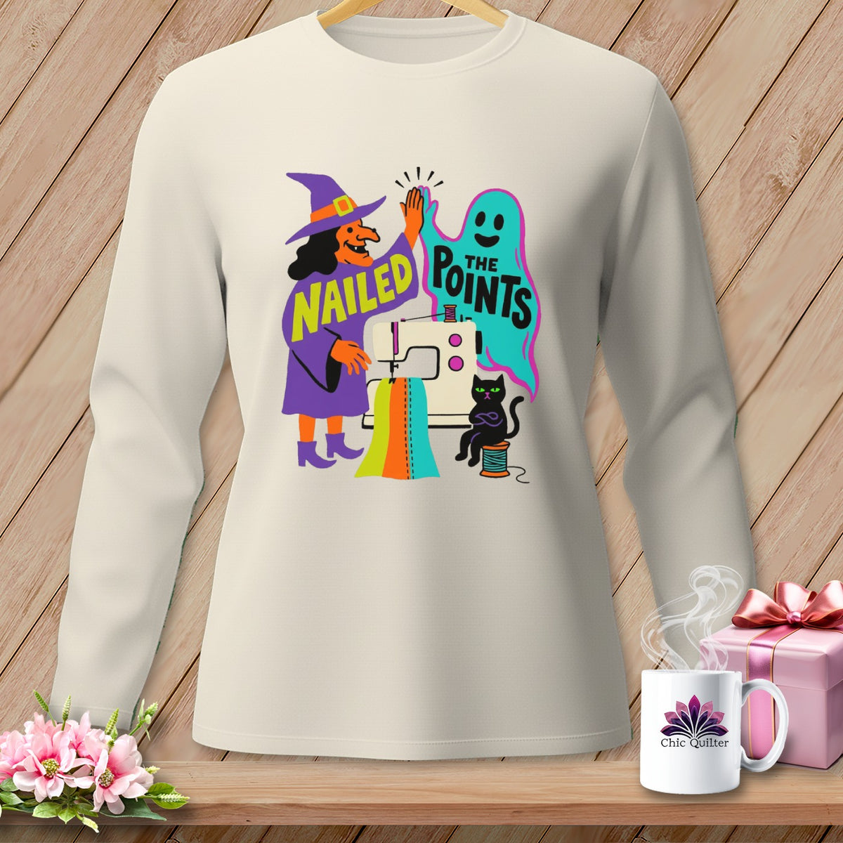 Cream long-sleeve shirt with graphic of witch, ghost, sewing machine, and cat saying "Nailed The Points".