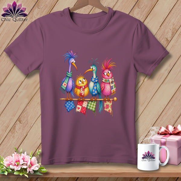 Purple crewneck t-shirt featuring a colorful cartoon illustration of four birds sitting on a knitting needle.