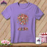 A purple crewneck t-shirt featuring an illustration of a whimsical girl holding folded quilts.