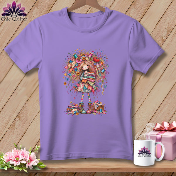 A purple crewneck t-shirt featuring an illustration of a whimsical girl holding folded quilts.