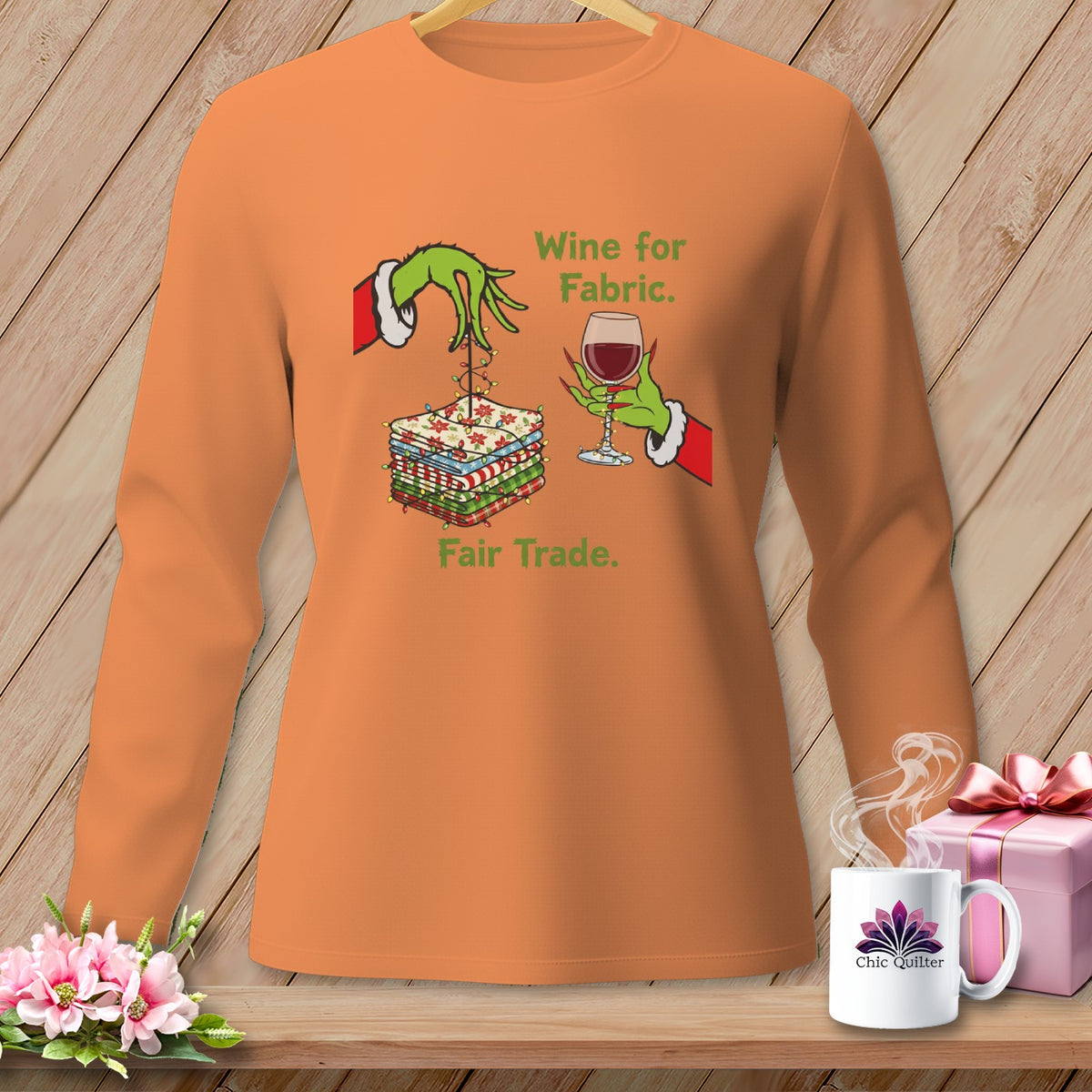 Orange long-sleeve shirt with Grinch hands holding fabric and wine, text reads "Wine for Fabric. Fair Trade."