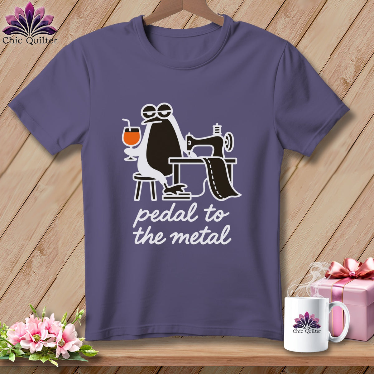 Purple t-shirt with a cartoon penguin sewing and holding a drink, text "pedal to the metal".