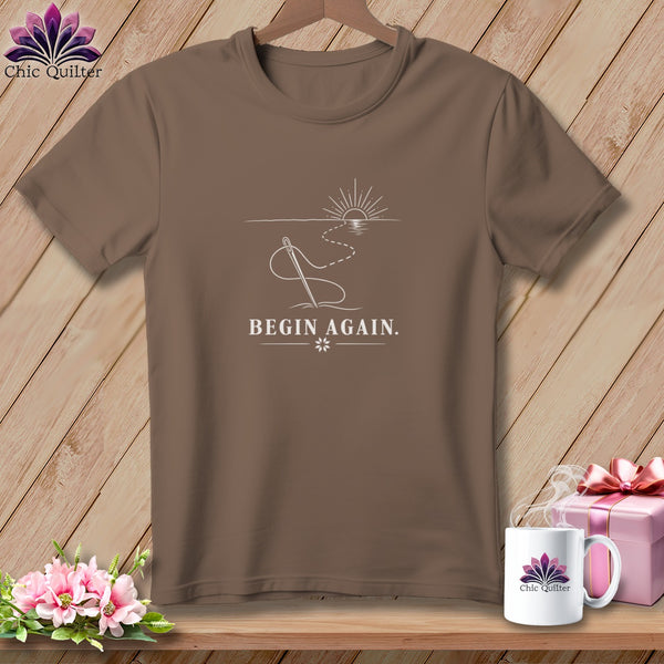 Brown t-shirt with needle, thread, and sunrise graphic with text "BEGIN AGAIN."