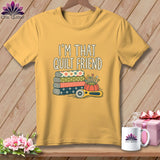 Yellow crewneck t-shirt featuring the text I AM THAT QUILT FRIEND above stacked patterned fabrics and sewing tools.