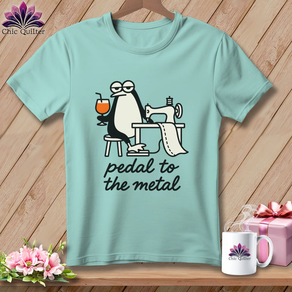 Light blue t-shirt with a cartoon penguin sewing and holding a drink, text reads "pedal to the metal".