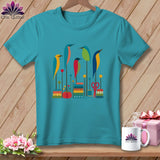 A teal crewneck t-shirt featuring a colorful graphic of stylized birds, spools, and sewing notions.