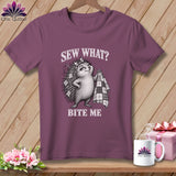 Mauve t-shirt hanging on a wooden background, featuring a hedgehog graphic with the text Sew What? Bite Me.