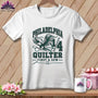 A white t-shirt hanging on a wooden background features a graphic with an eagle holding a needle, the text "PHILADELPHIA QUILTER FIRST & SEW," and the number 14.