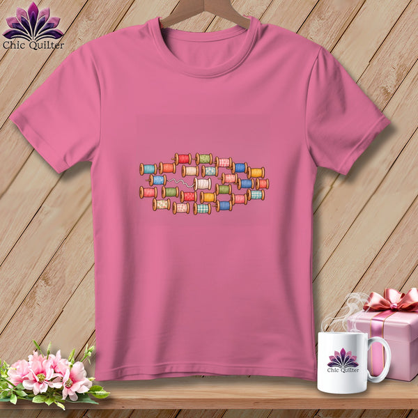 Pink crewneck t-shirt featuring a colorful graphic of stacked wooden spools of thread.