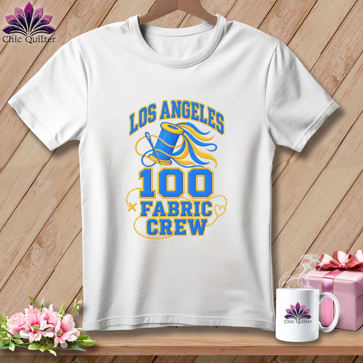 White t-shirt with blue and yellow Los Angeles 100 Fabric Crew graphic on a wooden background.