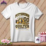 White t-shirt with a black and gold Pittsburgh Quilter graphic featuring sewing supplies against a wooden background.