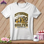 White t-shirt with a black and gold Pittsburgh Quilter graphic featuring sewing supplies against a wooden background.