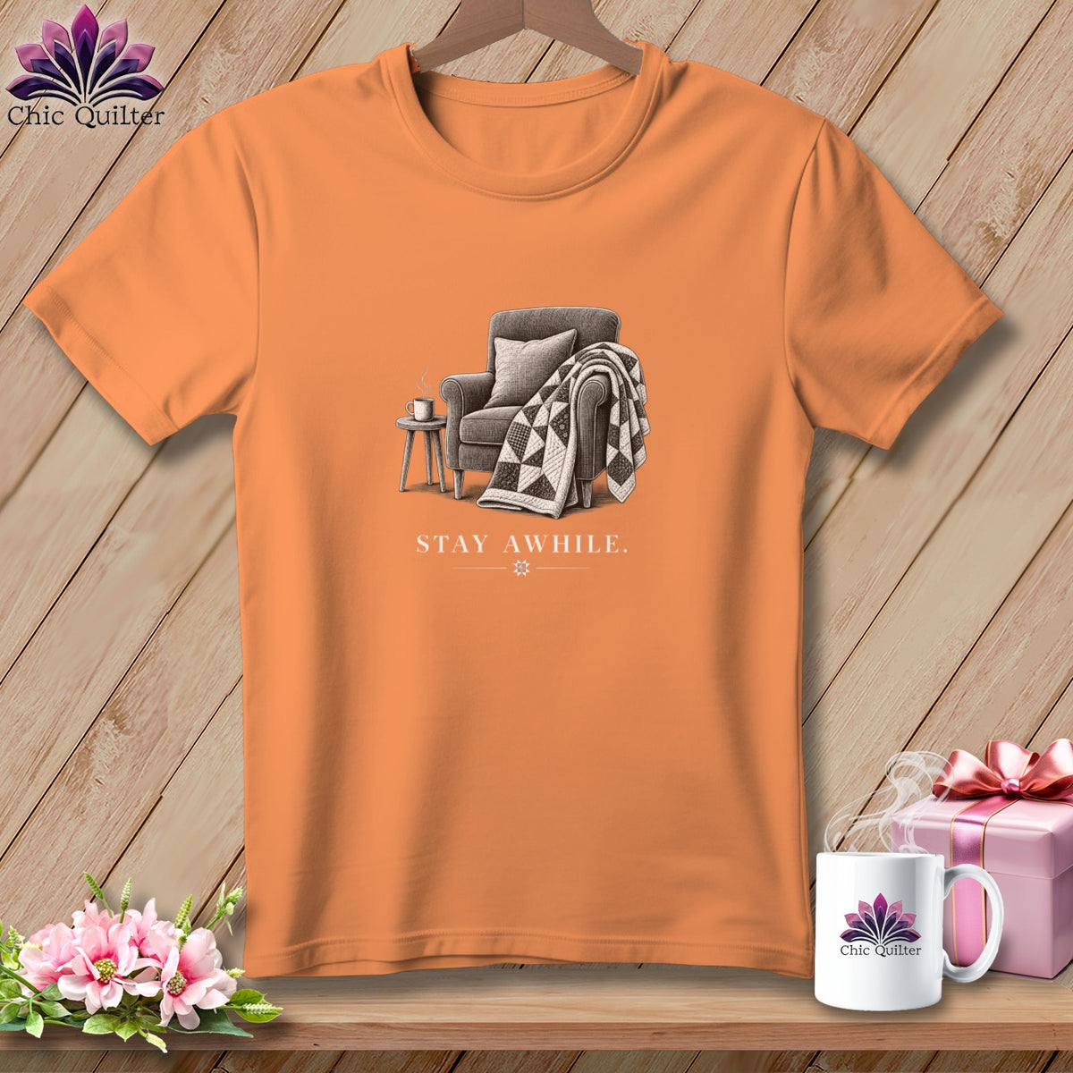 Orange t-shirt with a graphic of an armchair, quilt, side table, and the text "STAY AWHILE."