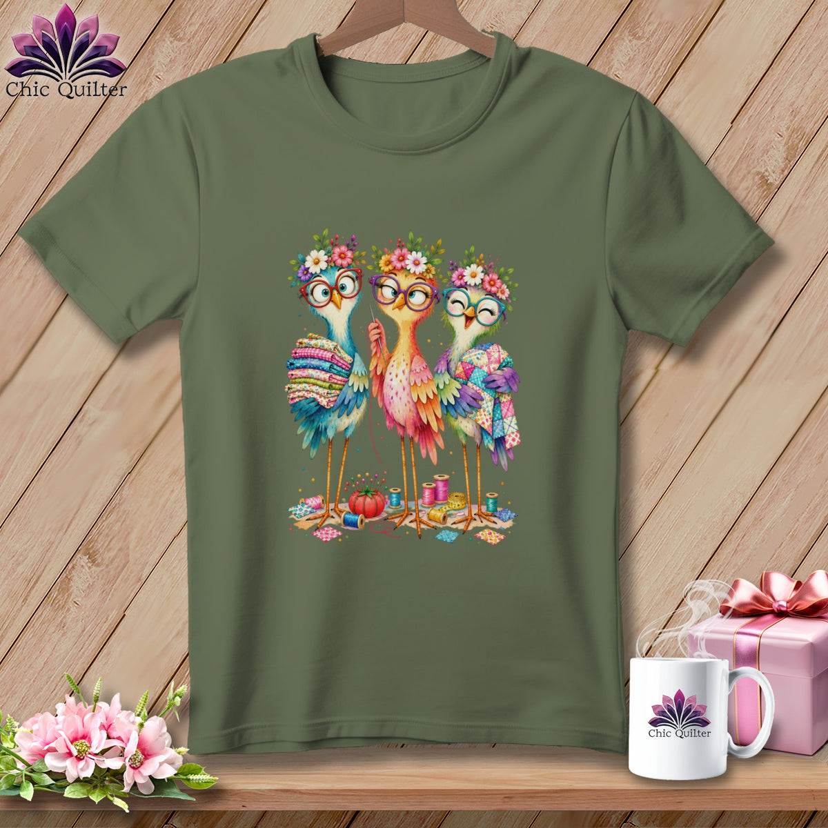 Olive green t-shirt featuring an illustration of three cute, bespectacled birds holding quilts amidst sewing supplies.