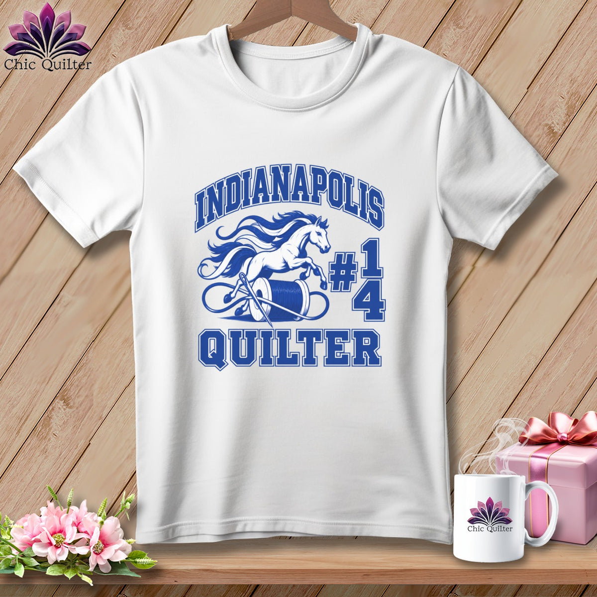 White t-shirt with blue graphic featuring a running horse, thread spool, needle, and text reading Indianapolis Quilter.