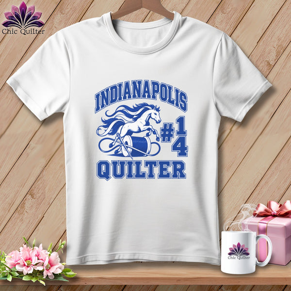 White t-shirt with blue graphic featuring a running horse, thread spool, needle, and text reading Indianapolis Quilter.