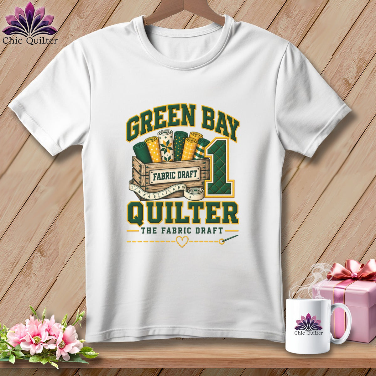 A white t-shirt features a Green Bay Quilter graphic with fabric bolts in a crate.
