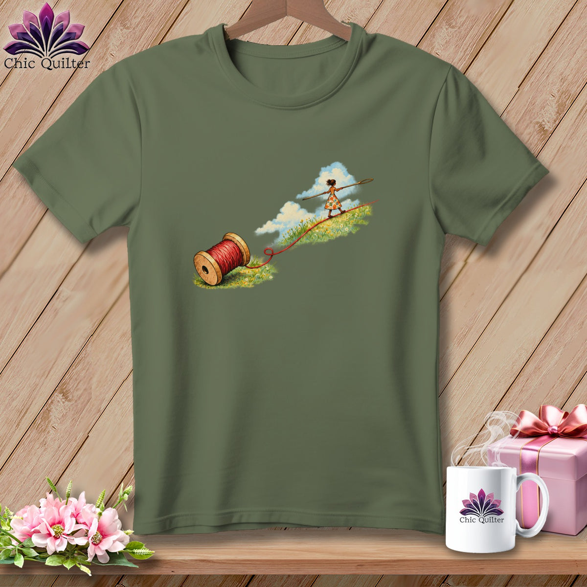 An olive green t-shirt featuring an illustration of a figure tightrope walking on red thread.