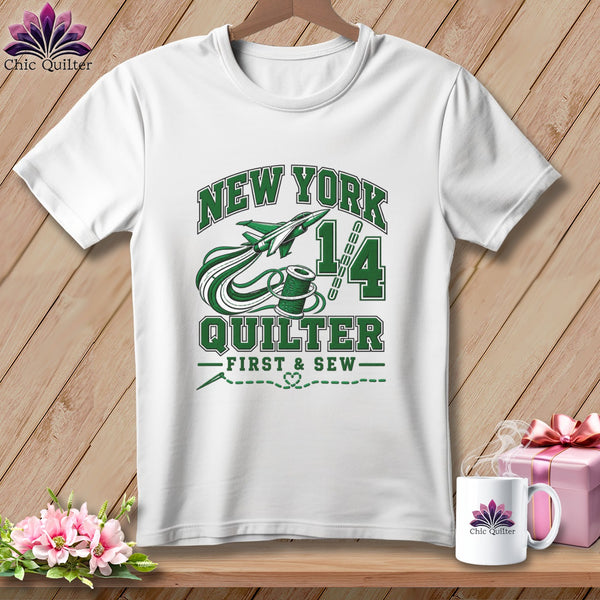 A white t-shirt hanging on a wooden background, featuring green text reading "New York Quilter" with airplane and spool graphics.