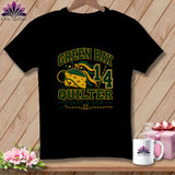 A black t-shirt hangs on a wooden hanger featuring Green Bay Quilter text and sewing-themed cheese graphic.