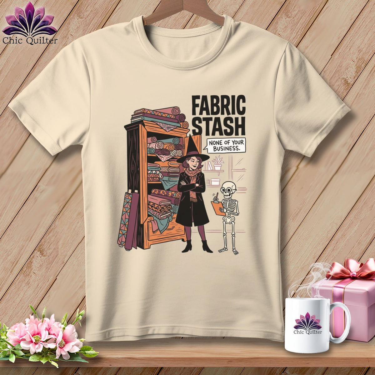 T-shirt graphic: Witch with fabric stash, skeleton, text "Fabric Stash None of Your Business."