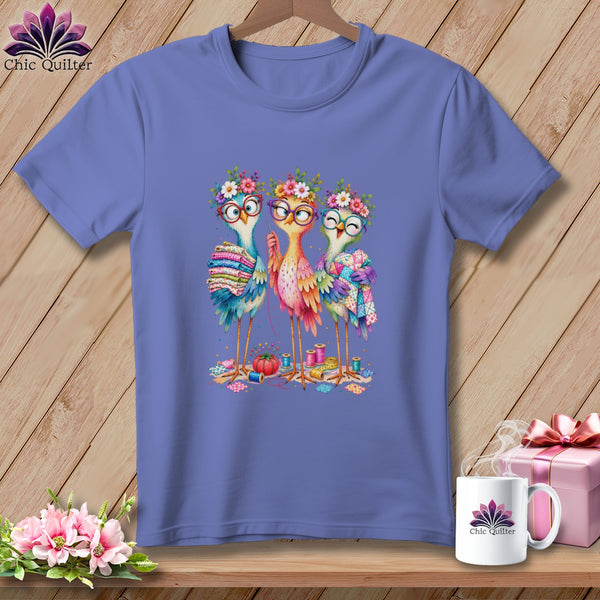 Periwinkle crewneck t-shirt featuring a colorful graphic of three quirky, bespectacled birds sewing with quilts.