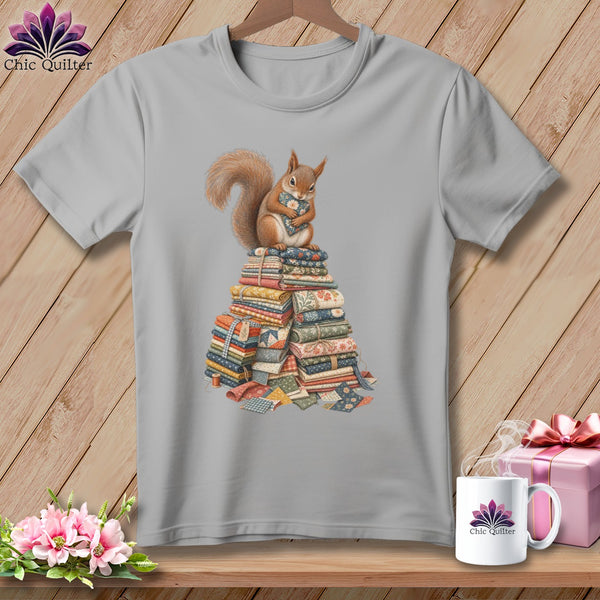 Gray t-shirt with a squirrel hugging a heart on a stack of fabric.
