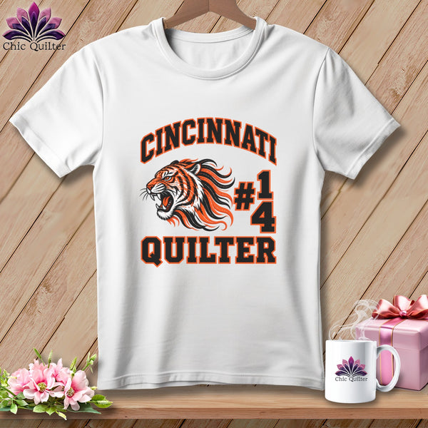 A white t-shirt hanging on a wooden background, featuring the text Cincinnati Quilter and a tiger graphic.