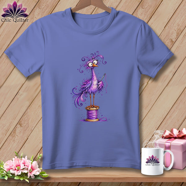 A purple t-shirt featuring a quirky purple bird standing on a spool of thread.