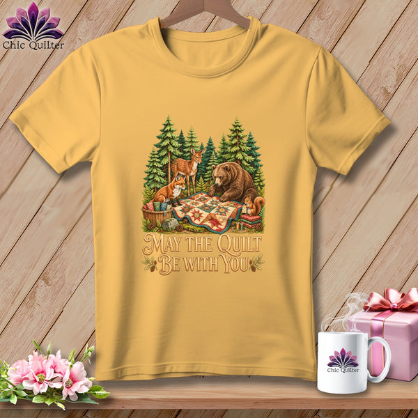 Gold t-shirt featuring a woodland scene with a bear, deer, fox, and squirrel gathered around a colorful quilt.