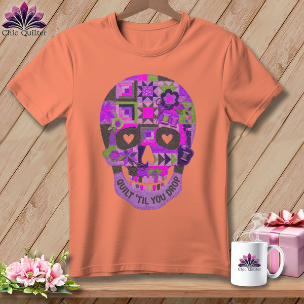 Peach t-shirt with a purple quilt-patterned skull graphic and "Quilt 'til You Drop" text.