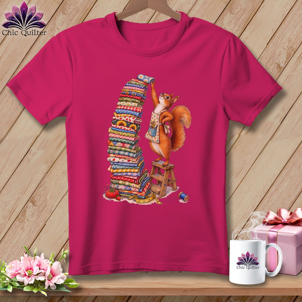 T-shirt graphic: squirrel with apron stacking colorful fabric bolts on a ladder.