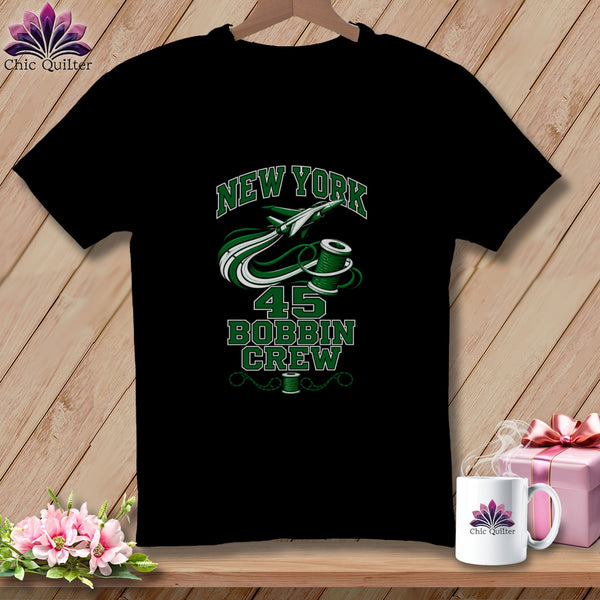 A black t-shirt featuring a green graphic with a jet, thread spool, and text reading "NEW YORK 45 BOBBIN CREW".