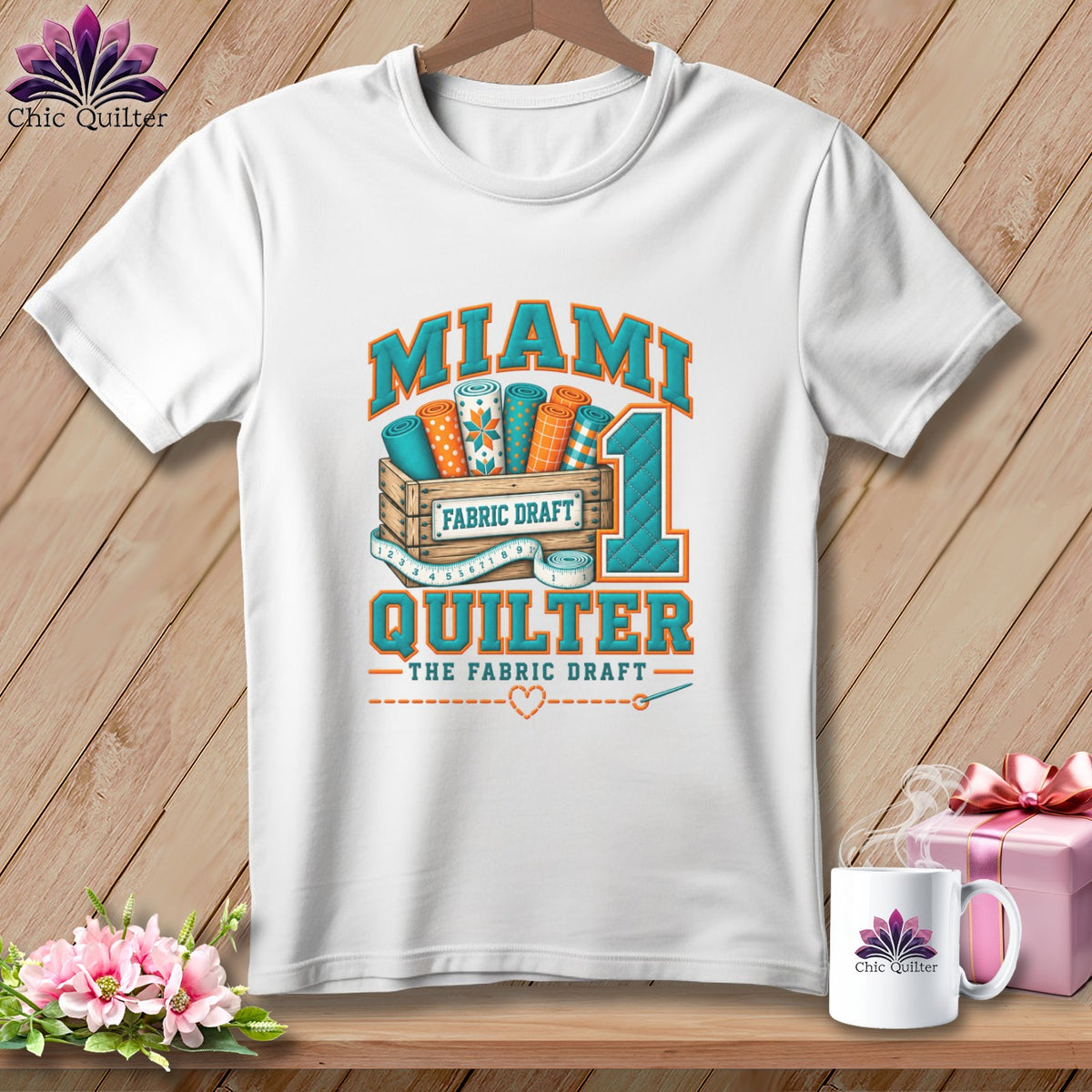 A white t-shirt hanging against a wooden wall features graphic text reading "MIAMI QUILTER" with fabric rolls.