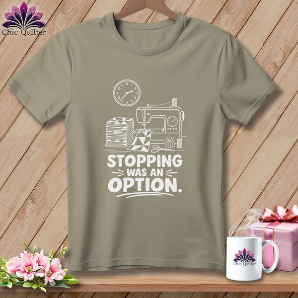 Khaki t-shirt with white graphic of sewing machine, fabric, and text "Stopping Was An Option."
