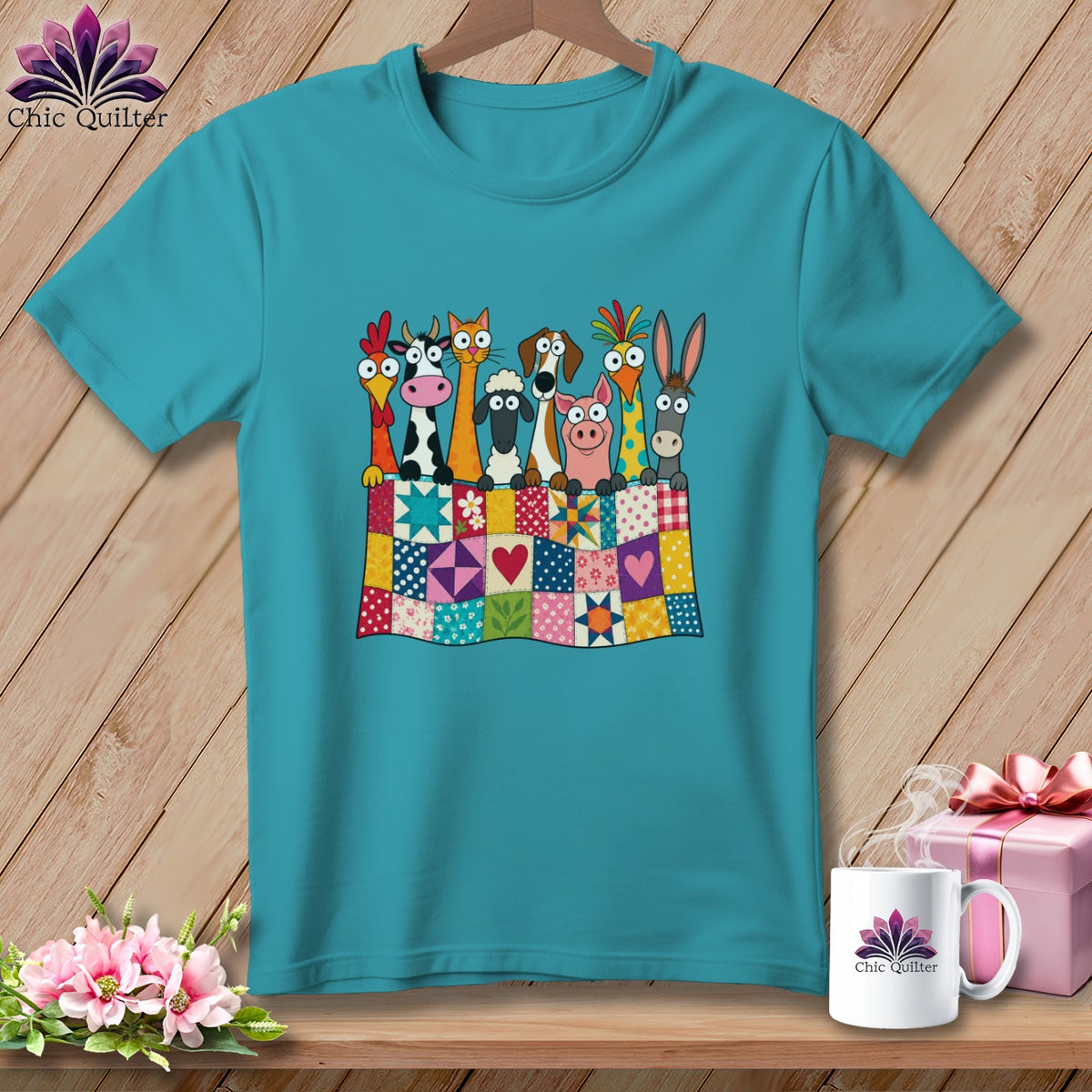 A turquoise t-shirt displays a graphic of cartoon farm animals peeking over a colorful patchwork quilt.