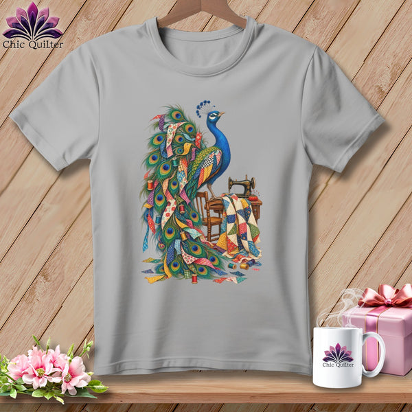 Gray t-shirt with a vibrant peacock design surrounded by quilting materials and a sewing machine.