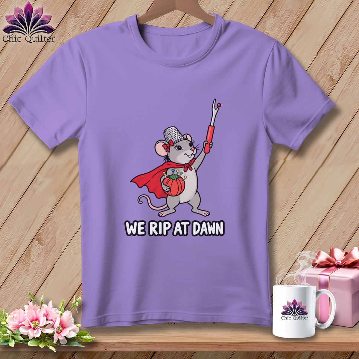 A purple t-shirt featuring a graphic of a mouse wearing a cape and holding a seam ripper, with the text WE RIP AT DAWN.