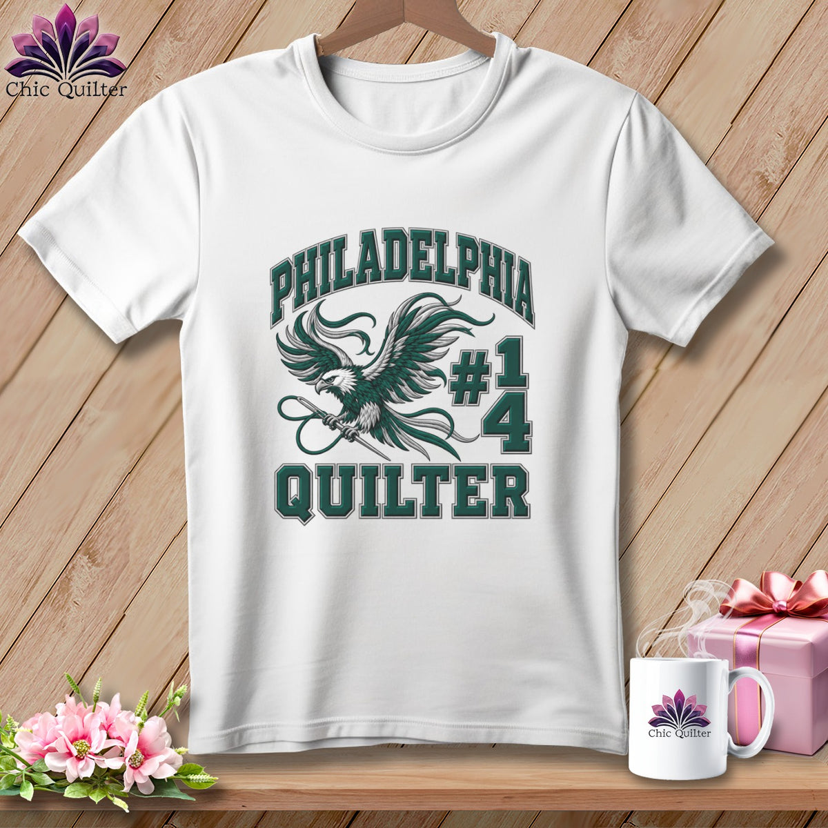 A white t-shirt hanging on a wooden background features a green eagle graphic and the text "Philadelphia #1 Quilter".