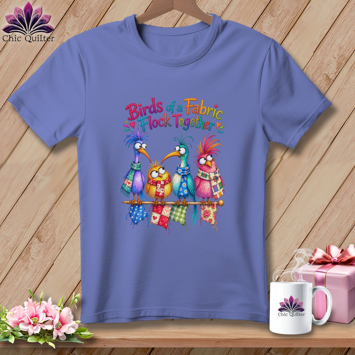 Periwinkle t-shirt featuring a colorful graphic of four whimsical cartoon birds and text reading "Birds of a Fabric Flock Together."
