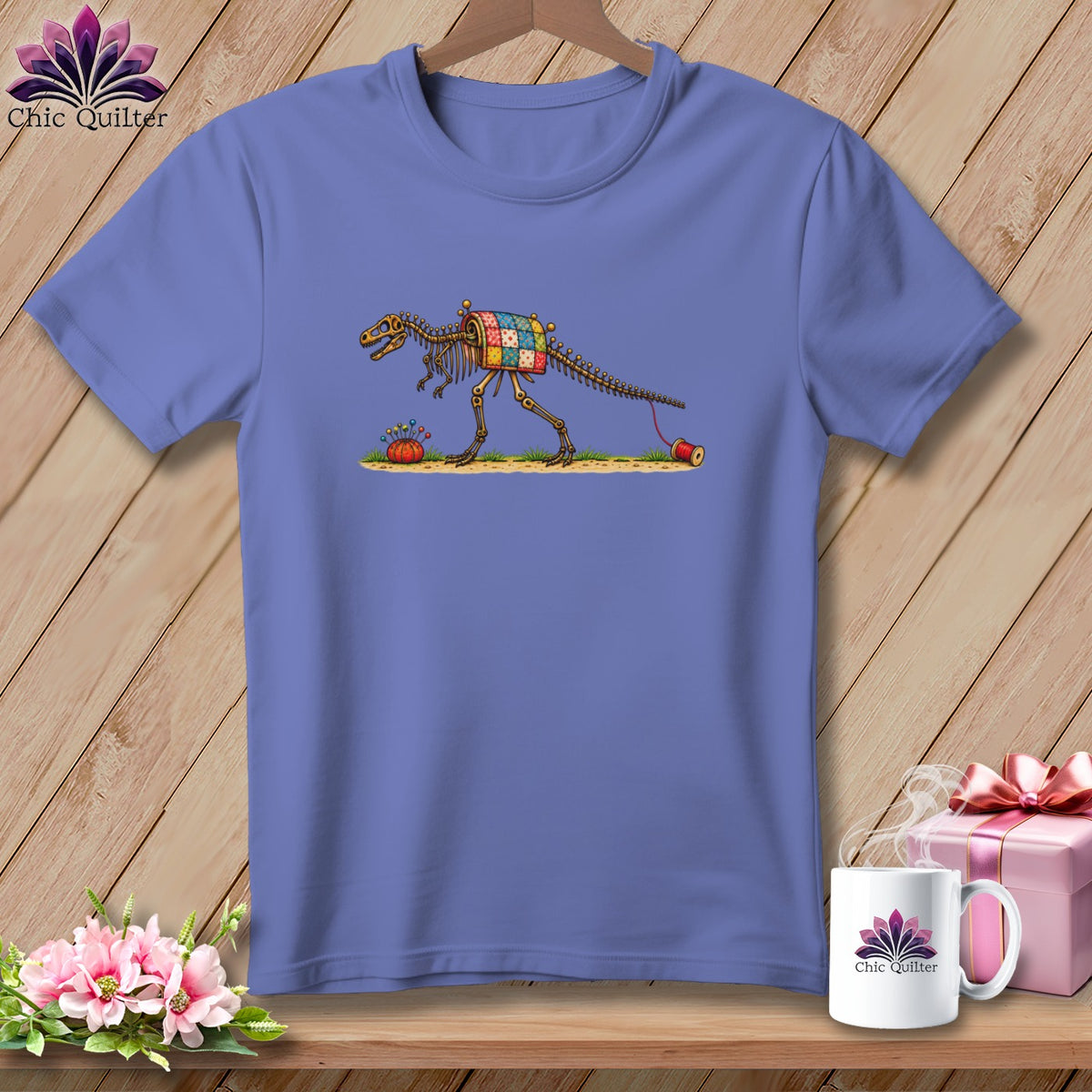 A periwinkle t-shirt featuring an illustration of a dinosaur skeleton with a patchwork quilt body on a wooden background.