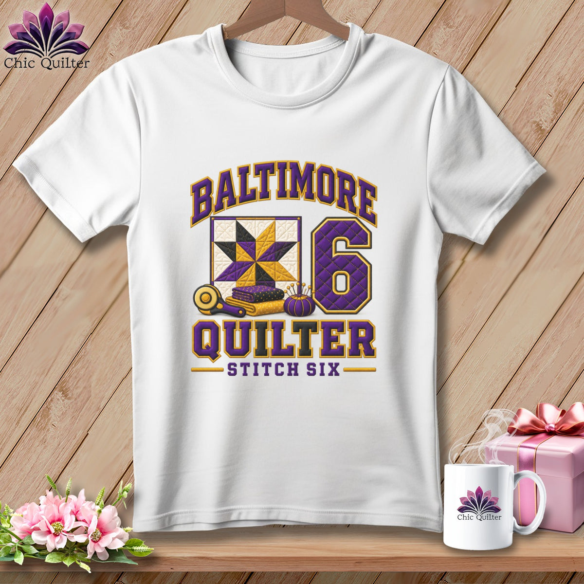 White t-shirt hanging on a wooden background, featuring purple and yellow quilting-themed graphics and text.