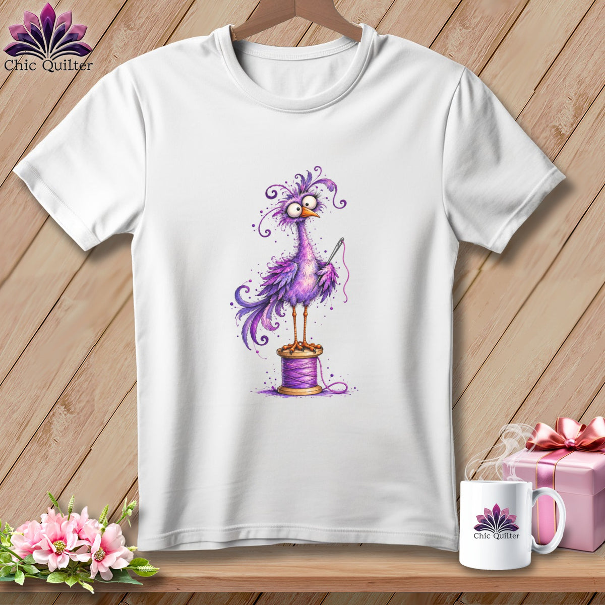 A white t-shirt hanging on a wooden wall displays a graphic of a whimsical purple bird standing on a thread spool.