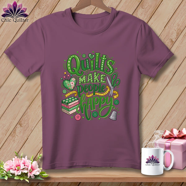 Plum t-shirt featuring green "Quilts make people happy" typography, stacked fabrics, and sewing motifs.