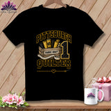 A black short-sleeve t-shirt features a graphic with yellow text reading Pittsburgh Quilter, a wooden crate of fabric rolls, a measuring tape, and a number one.