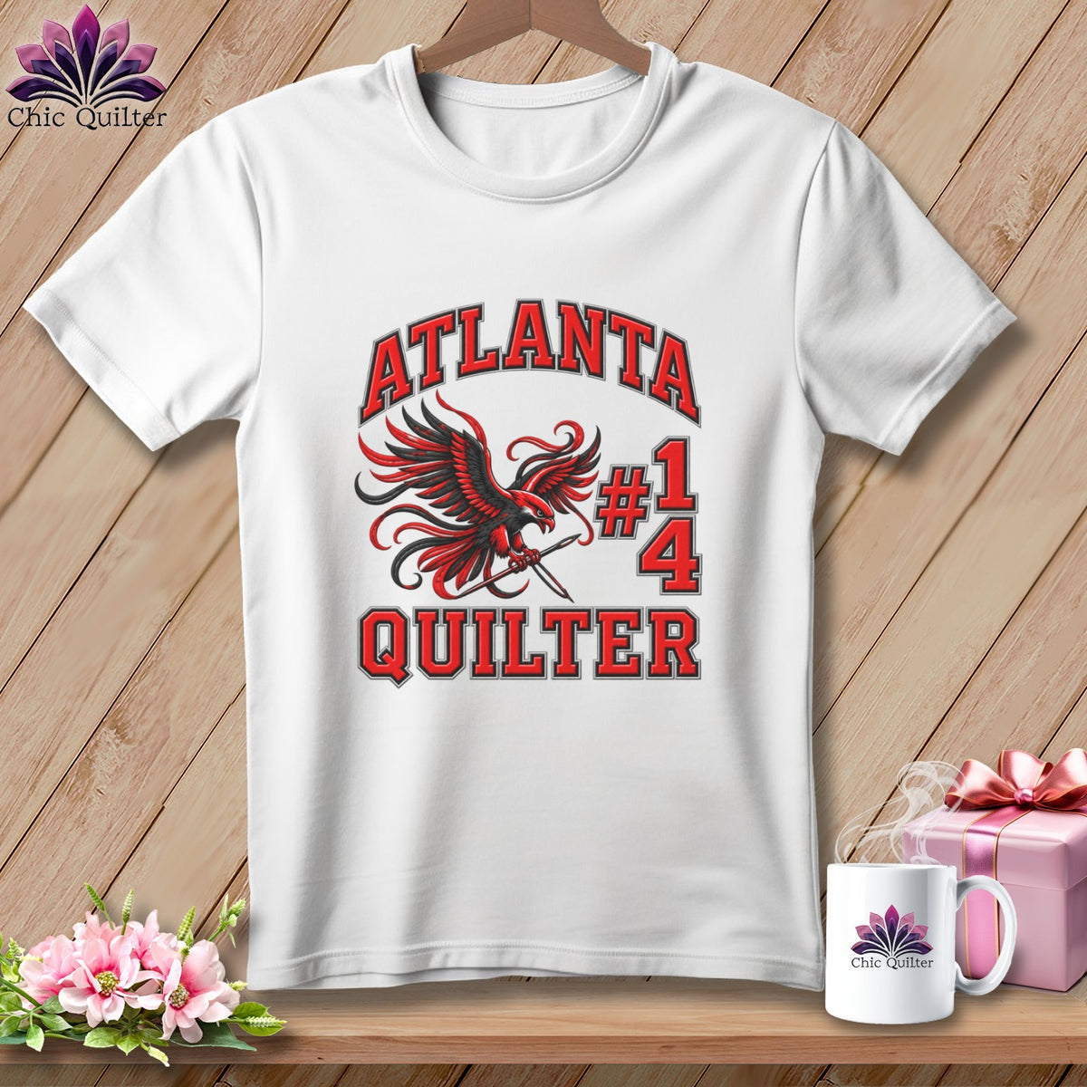 White t-shirt featuring a red and black falcon graphic holding a needle, with text reading Atlanta Quilter #14.