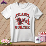 White t-shirt featuring a red and black falcon graphic holding a needle, with text reading Atlanta Quilter #14.