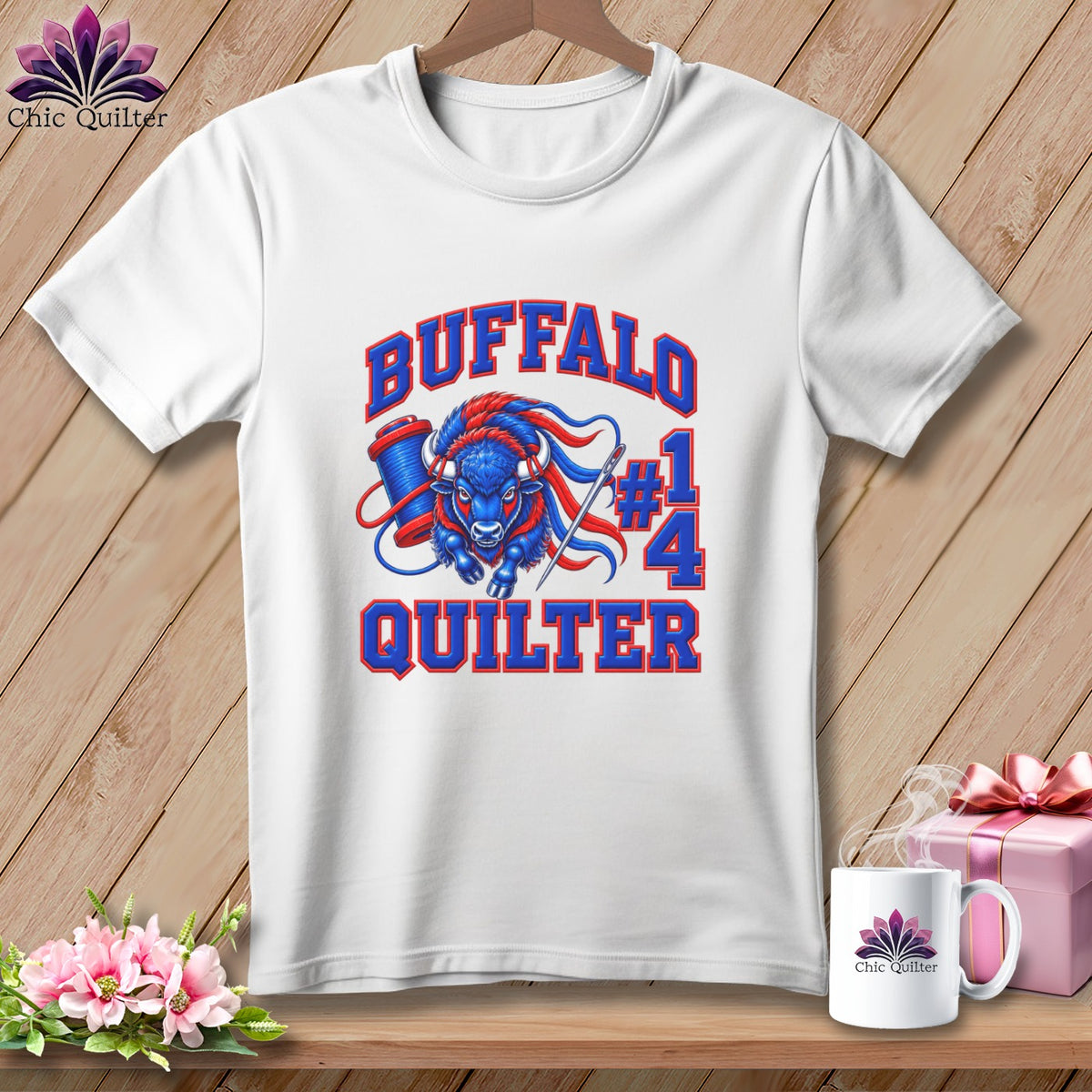 A white t-shirt hanging on a wooden background, featuring a graphic of a blue buffalo, sewing supplies, and the text "Buffalo Quilter #14."